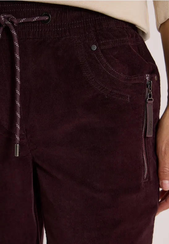 Nahaufnahme einer bordeauxfarbenen Cordhose mit Tunnelzugbund und seitlicher Reißverschlusstasche.