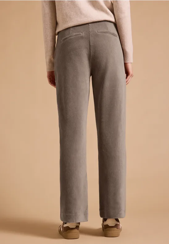 Vue de dos d’une personne portant un pantalon gris large et des chaussures beiges devant un fond neutre.