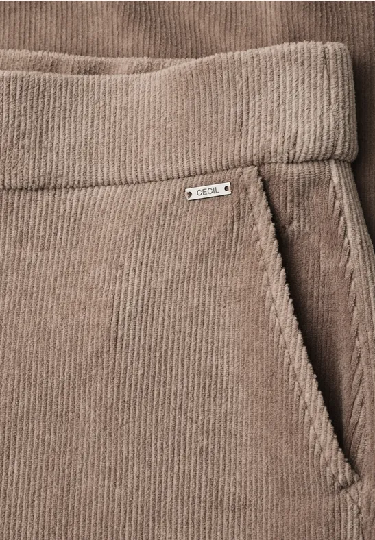 Pantalon en velours côtelé beige avec taille élastique et poche latérale ornée d'une petite étiquette métal.