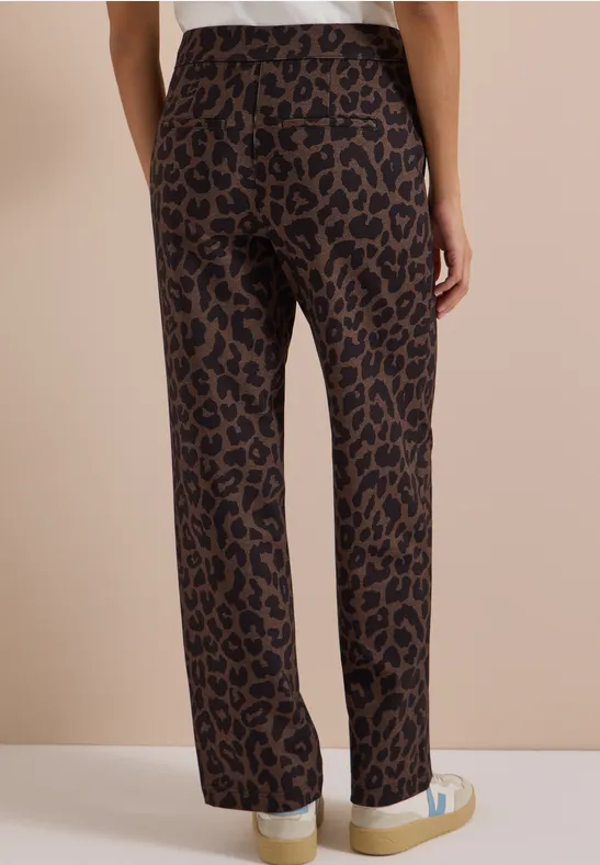 Person von hinten: braune, gerade geschnittene Hose mit Leopardenmuster und weißen Sneakern.