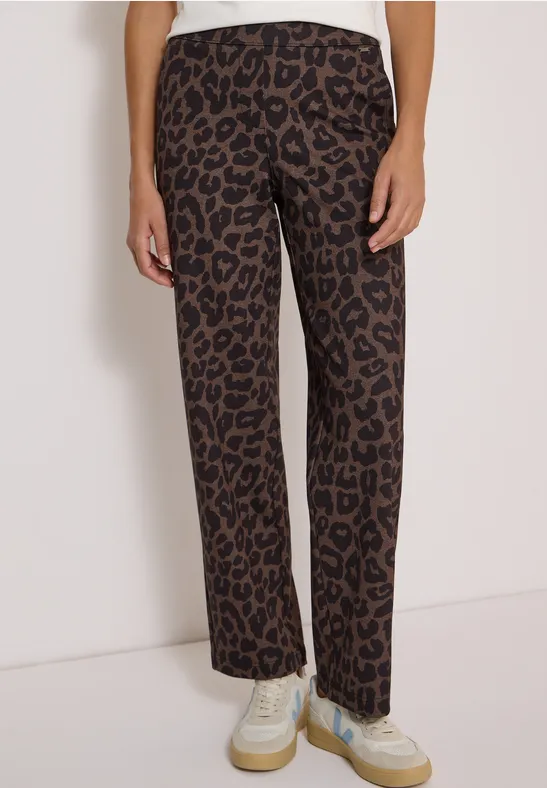 Frau trägt weite braune Hose mit Leopardenmuster und weiße Sneaker.