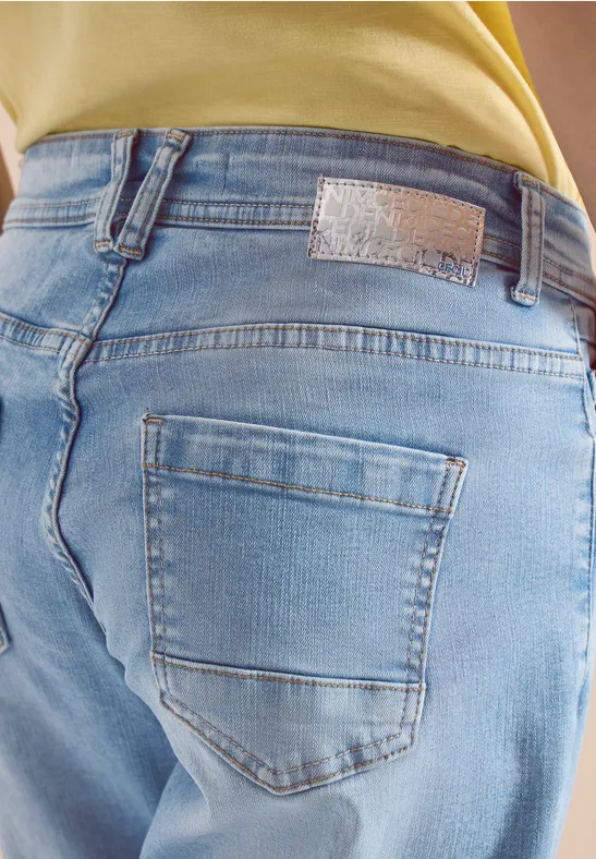 Een persoon draagt lichtblauwe jeans van achteren gefotografeerd, met achterzak en gele top.