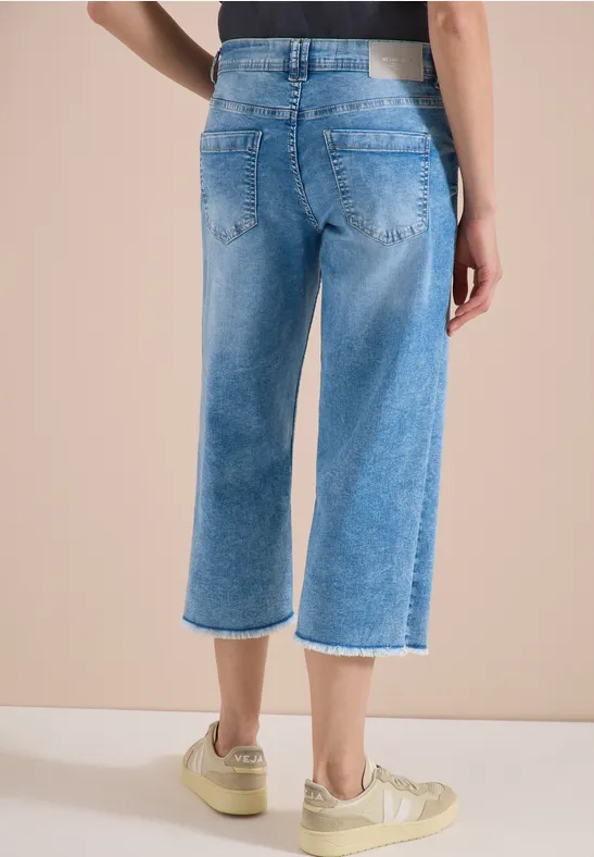 Achteraanzicht van een persoon in lichtblauwe, wijde cropped jeans met rafelige zoom en beige sneakers