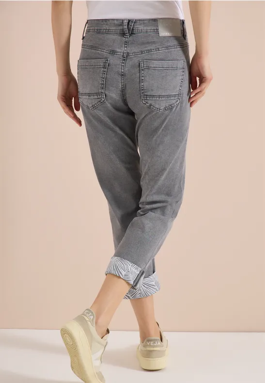 Rugaanzicht van een persoon in grijze omgezoomde spijkerbroek en sneakers voor een neutrale achtergrond