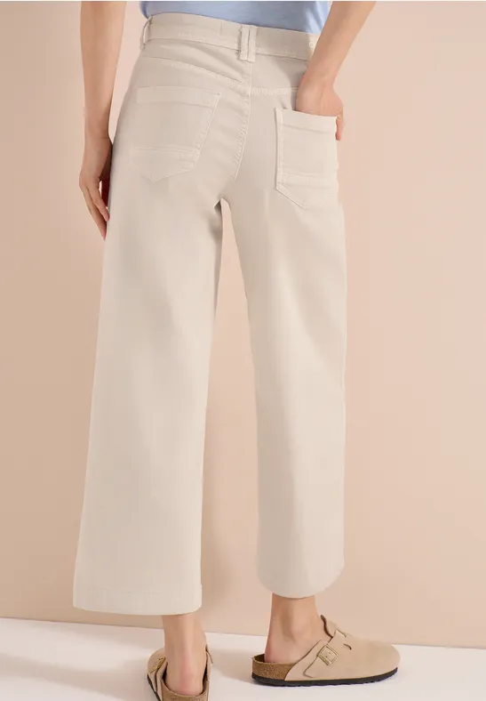 Pantalon large beige taille haute avec poches plaquées, porté avec des sabots beiges.