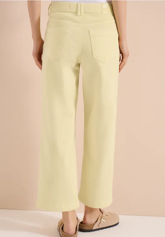 Rückenansicht einer Person in pastellgelben, weiten Jeans mit aufgesetzten Taschen vor beigem Hintergrund.