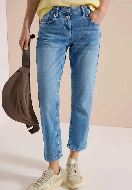 Une personne porte un jean bleu, des baskets beige clair et tient un sac marron.