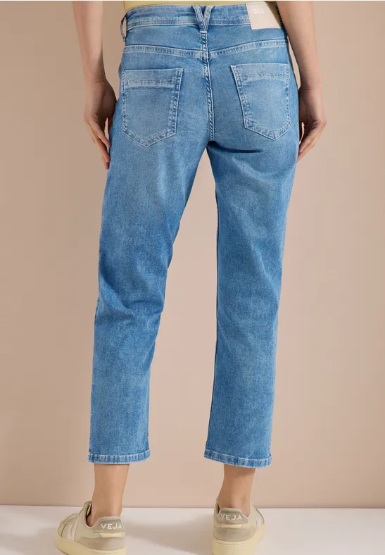 Femme vue de dos portant un jean bleu clair et des baskets beiges