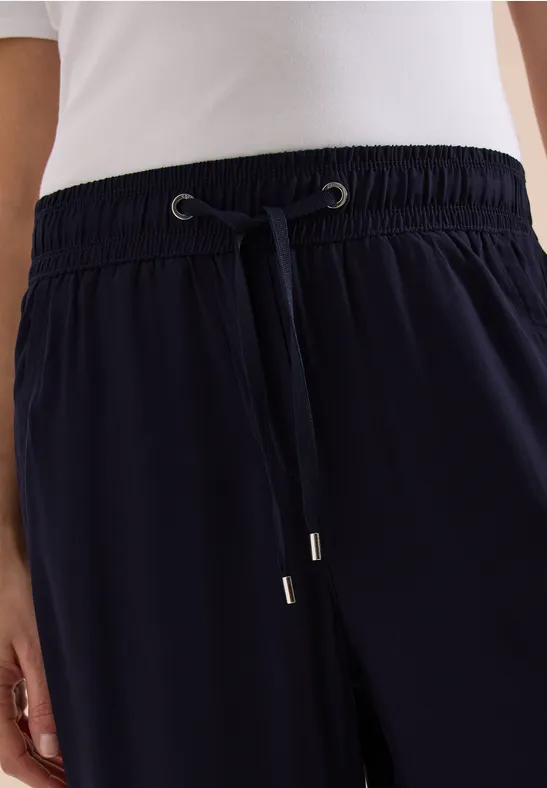 Nahaufnahme einer Person in marineblauen Hosen mit Tunnelzug und weißem Oberteil.