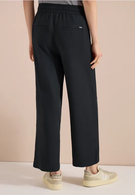 Rückansicht einer Person in locker sitzender, weiter schwarzer Hose mit elastischem Bund und Seitentaschen.