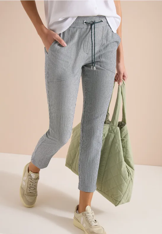 Persoon draagt grijze geruite broek met trekkoord, witte top, groene tas en lichte sneakers.