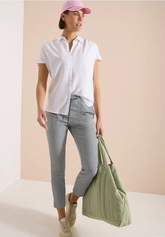 Dame in wit shirt, lichtblauwe jeans en sneakers, draagt een grote groene gewatteerde tas voor een neutrale achtergrond.