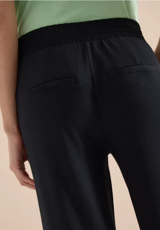 Rückansicht einer Person in dunkelblauen Hosen mit elastischem Bund und aufgesetzten Gesäßtaschen.