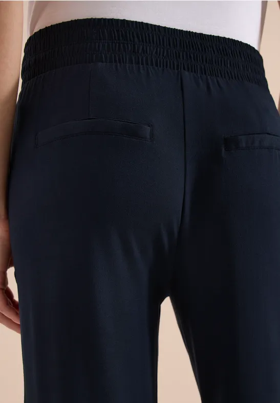 Rückenansicht einer Person in schwarzen Hosen mit elastischem Bund und zwei Paspeltaschen.