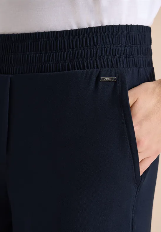 Hand steckt in der Seitentasche einer dunkelblauen Jogginghose mit elastischem Bund und kleinem Markenlogo.