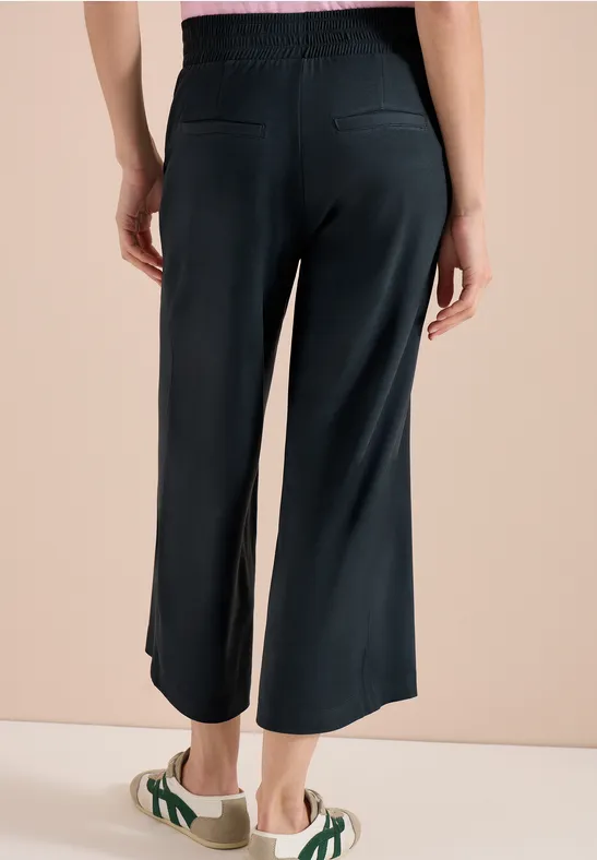 Frau von hinten in weiten, knöchellangen schwarzen Hosen und grünen Sandalen.