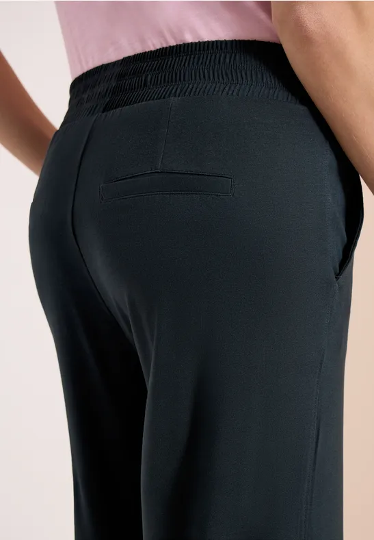 Detailaufnahme eines von hinten fotografierten Modells in schwarzen Hosen mit Gesäßtasche und seitlichen Eingrifftaschen.