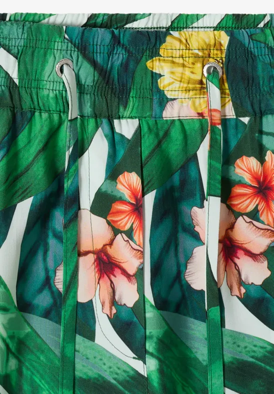 Grüne Badeshorts mit tropischen Blättern und bunten Hibiskusblüten in Orange und Gelb.