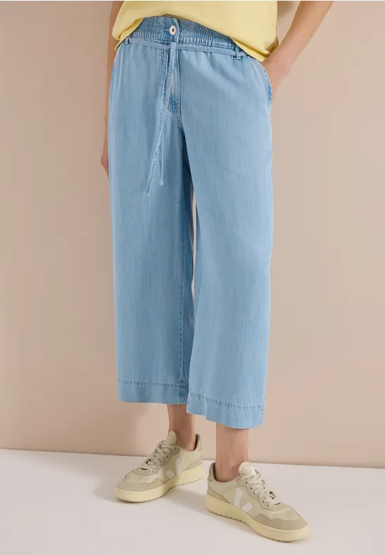 Losvallende lichtblauwe wijde jeans met koordsluiting tot de enkels, gecombineerd met beige sneakers.
