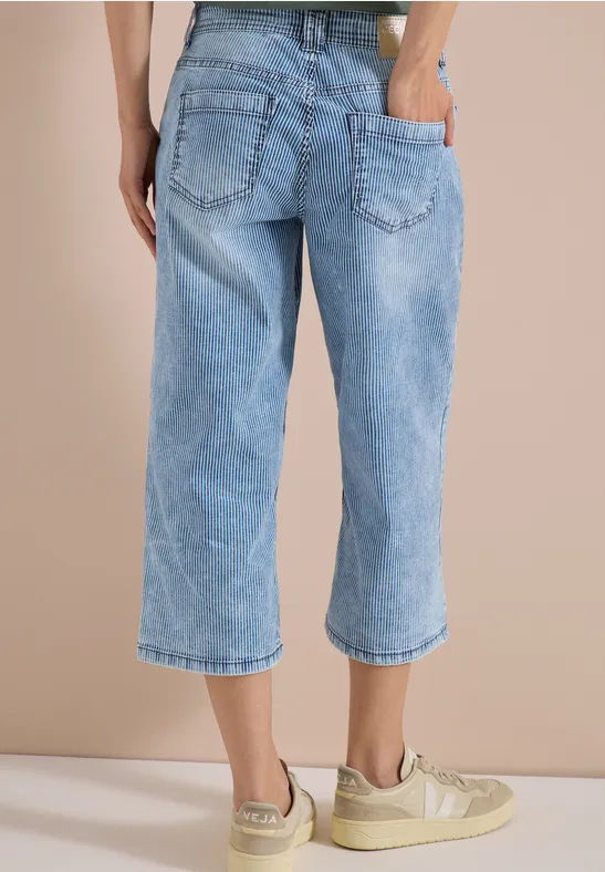 Helle, weite Jeans-Culotte bis zur Wadenmitte, kombiniert mit beige Sneakern.