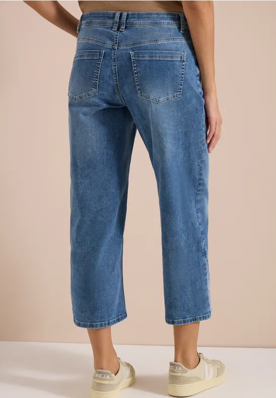 Rückansicht einer Person in blauen, hochgeschnittenen, weiten Cropped-Jeans und weißen Sneakers.