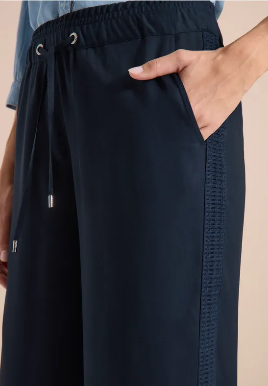Dunkelblaue Freizeithose mit elastischem Bund, seitlicher Ziernaht, Hand in Tasche.