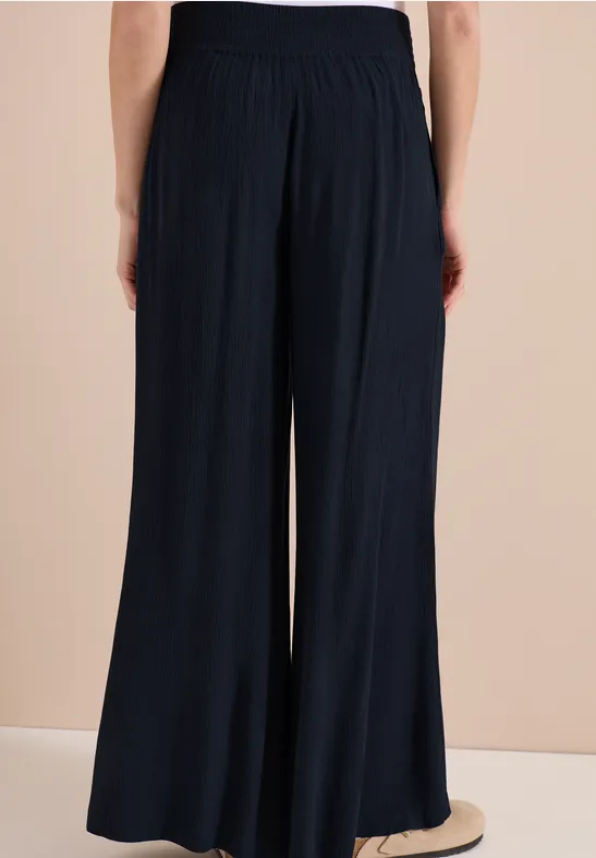 Person von hinten in einer dunkelblauen, weiten, fließenden Hose mit hohem Bund.