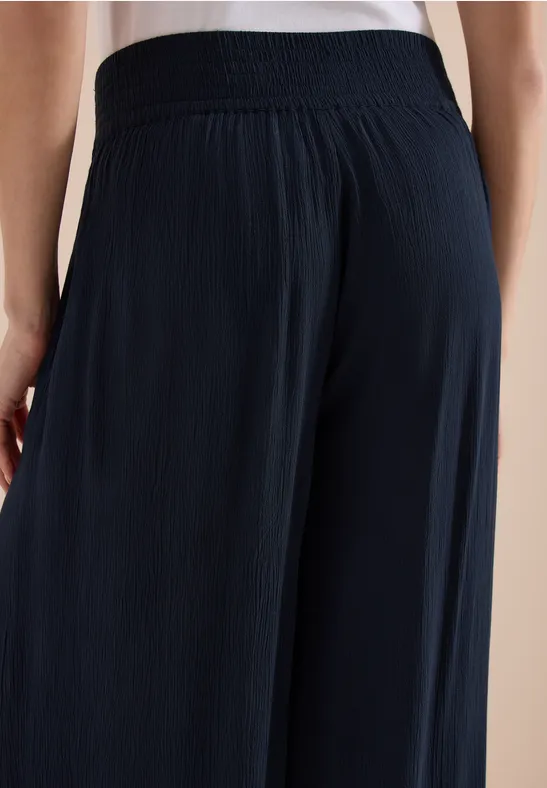 Dunkle, weite, plissierte Hose an einer weiblichen Person von hinten