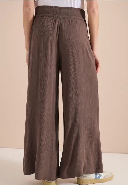 Rückansicht einer Person mit weitem, braunen, hochgeschnittenen Hosenrock und weißen Sneakers.