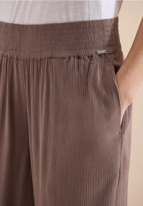 Detailaufnahme von braunen, plissierten Hosen mit seitlicher Tasche und weißem Oberteil.