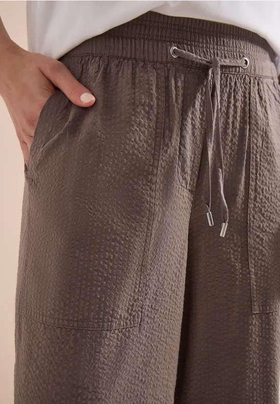 Nahaufnahme einer braunen, strukturierten Hose mit elastischem Bund, Tunnelzug und seitlicher Tasche.
