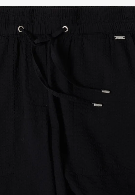 Schwarze Hose mit Waffelstruktur, elastischem Bund und Kordelzug mit silbernen Endstücken.