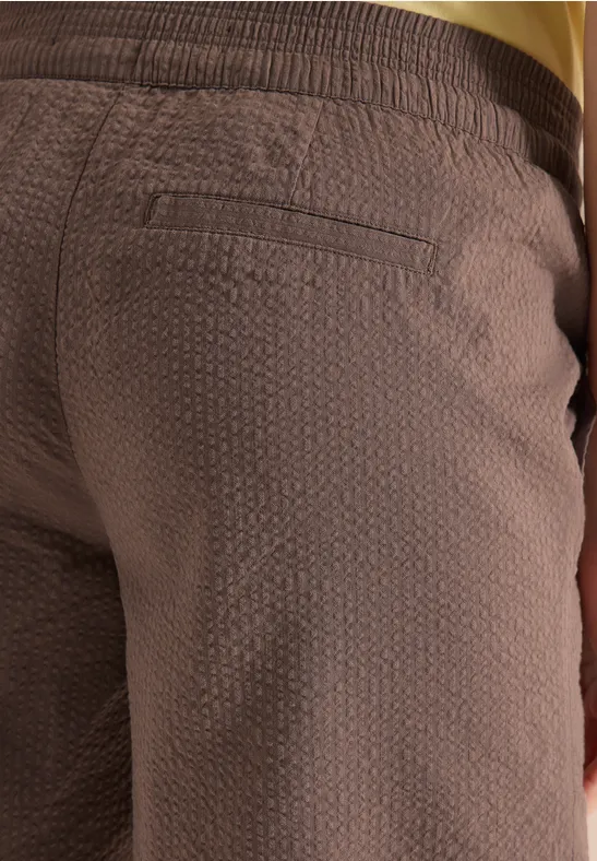 Nahaufnahme einer braunen, strukturierten Hose mit Gesäßstasche und goldenem Taillenbund.