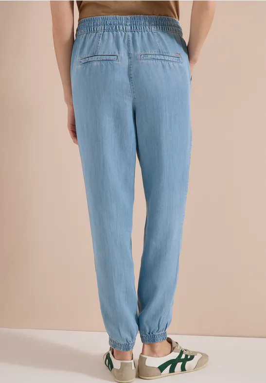 Achteraanzicht van een persoon in losse lichtblauwe joggingsbroek met elastische taille en witte sneakers.