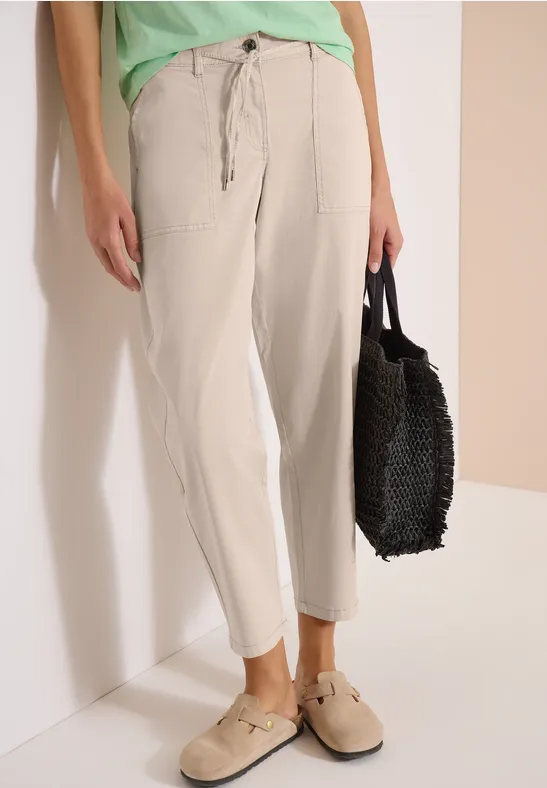 Eine Person trägt eine bequeme beige Hose mit großen Taschen, beigen Schuhen und hält eine schwarze Tasche.