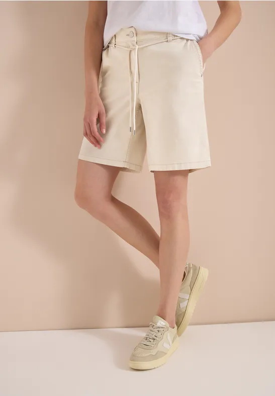 Persoon draagt wit T-shirt, knielange beige shorts en lichtgekleurde sneakers.