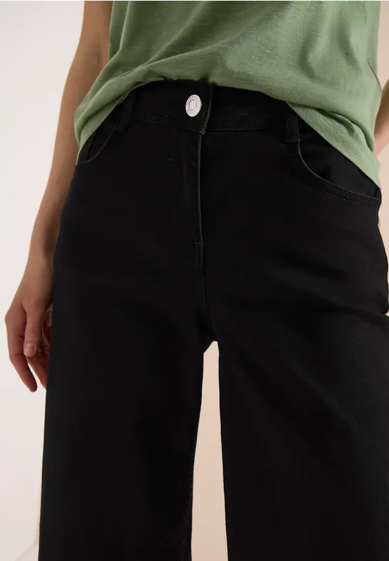 Schwarze, weite Hose mit hoher Taille und grünem Oberteil, frontalansicht.