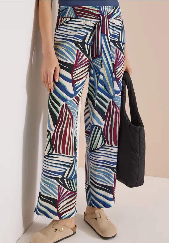 Pantalon large en tissu à motif de feuilles abstraites bleu, bordeaux et blanc, lien à la taille, accompagné d’un sac noir.