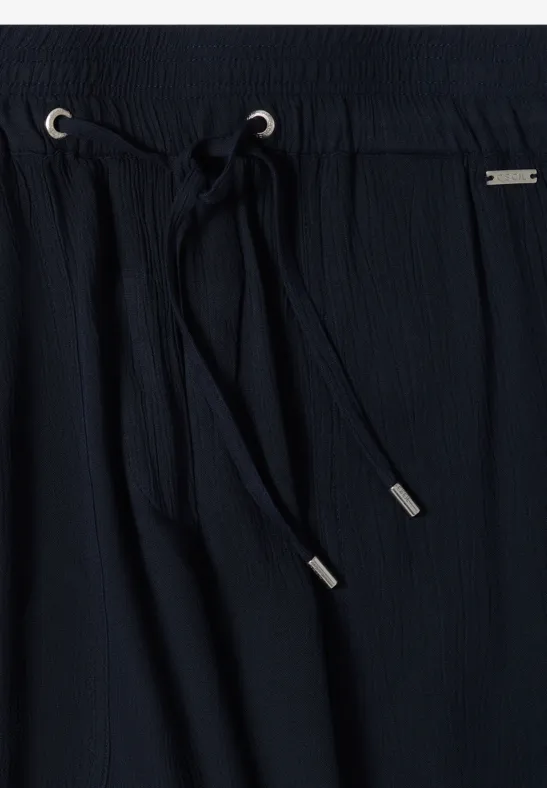 Close-up van een zwarte, gestructureerde broek met elastische taille en koord met zilverkleurige uiteinden.