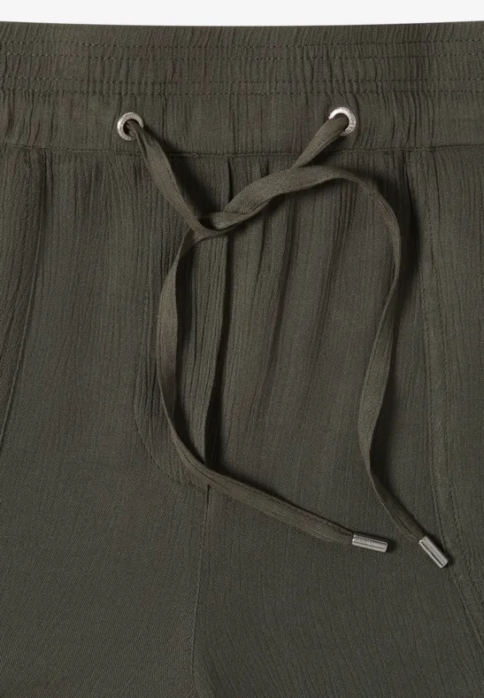 Close-up van een olijfgroene broekband van stof met elastische taille en trekkoord.