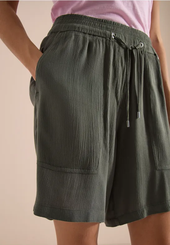 Olijfgroene korte broek met trekkoord, opgestikte zakken en fijne ribstructuur, losvallend tot net boven de knie.