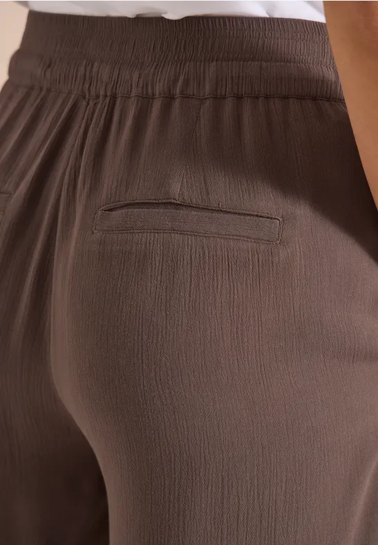 Close-up van een bruine, gestructureerde broek met elastische tailleband en achterzak.