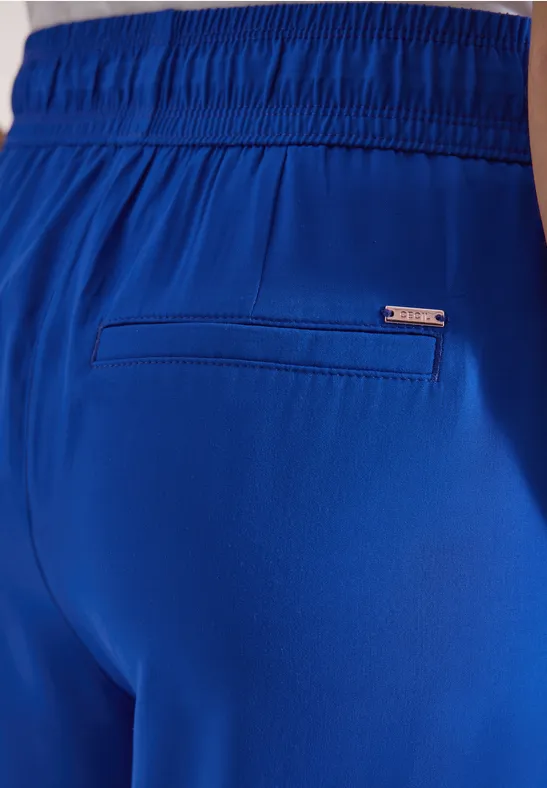 Close-up van een blauwe short met elastische taille, paspelzak en klein metalen merklabel.