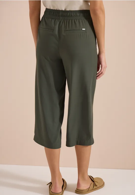 Vue de dos d'une personne portant un pantalon 3/4 vert foncé ample à taille élastique et mocassins beiges.