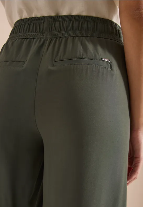 Gros plan d’une personne de dos, porte un pantalon kaki à taille élastique et poches arrière.