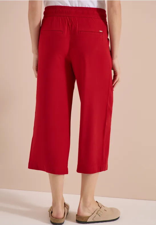 Rode, wijde 7/8-broek met elastische taille en achterzak, gecombineerd met beige instappers.