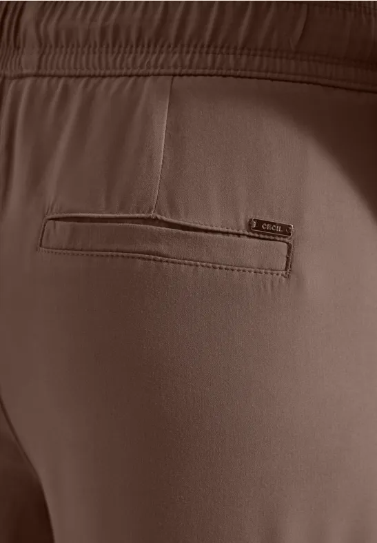 Close-up van de achterkant van een bruine broek met elastische taille en geïntegreerde ritszak.