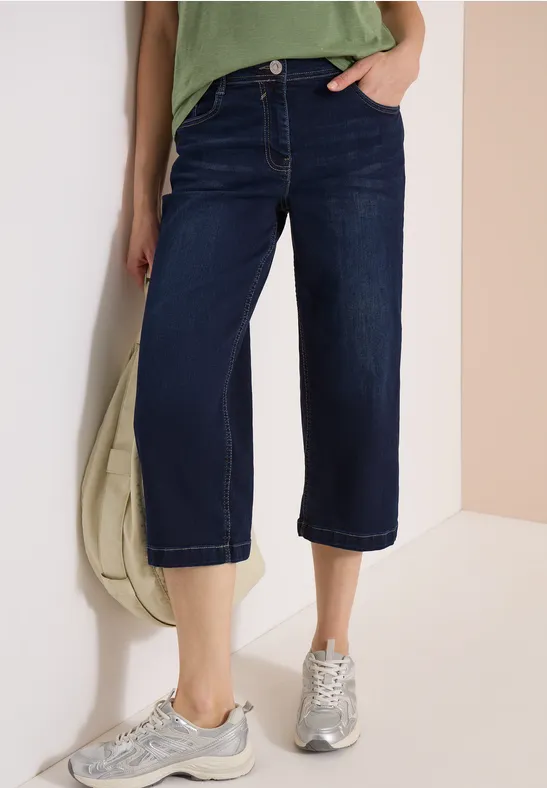 Damen-Jeans-Culotte aus dunklem Denim, weiter Schnitt, knöchellang, mit Sneakers kombiniert.