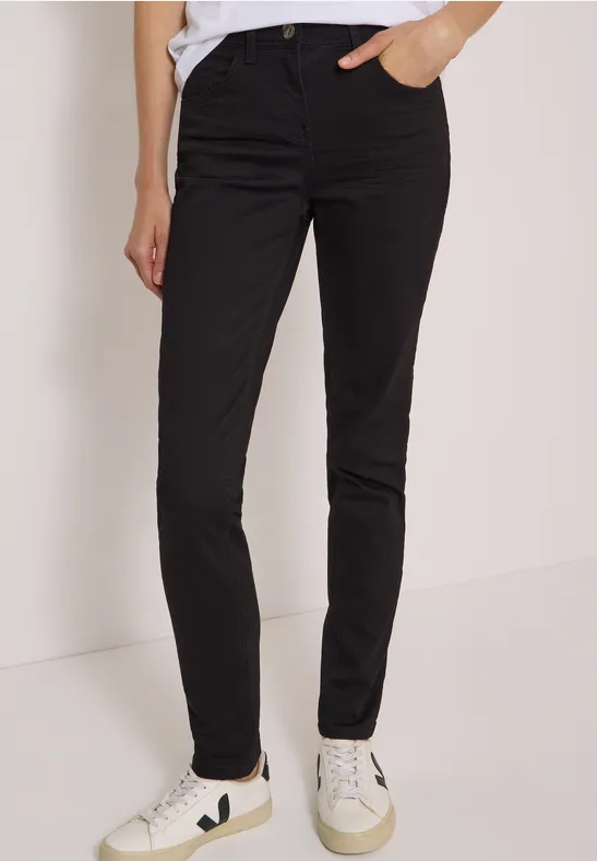 Pantalon noir ajusté jusqu’aux chevilles, porté avec des baskets blanches, sur fond neutre.