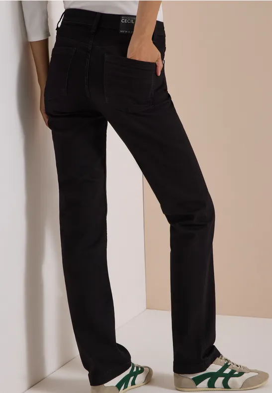 Jean noir coupe droite, porté avec des baskets blanches à détails verts.